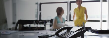 Festnetztelefon im Vordergrund, zwei Frauen unscharf im Hintergrund