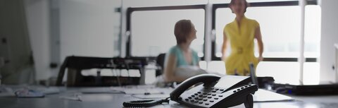 Festnetztelefon im Vordergrund, zwei Frauen unscharf im Hintergrund