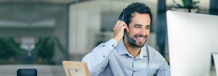 Mann im Büro mit Headset vor einem Bildschirm