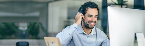 Mann im Büro mit Headset vor einem Bildschirm