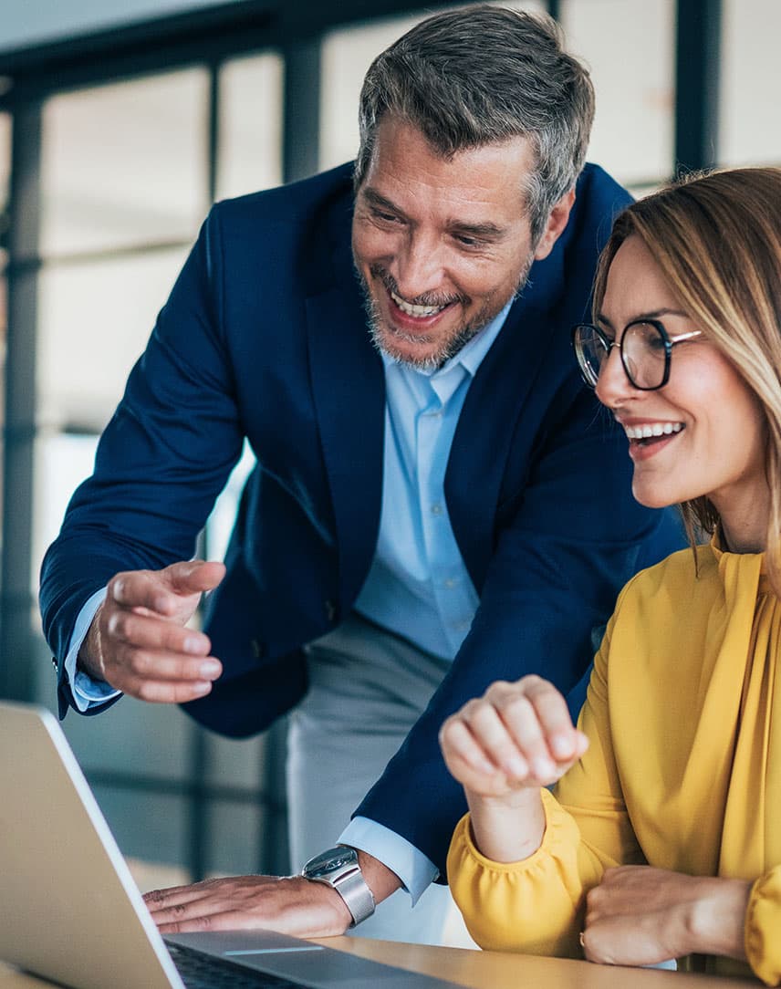 Mann und Frau im Business-Look schauen lachend auf einen Laptop-Bildschirm
