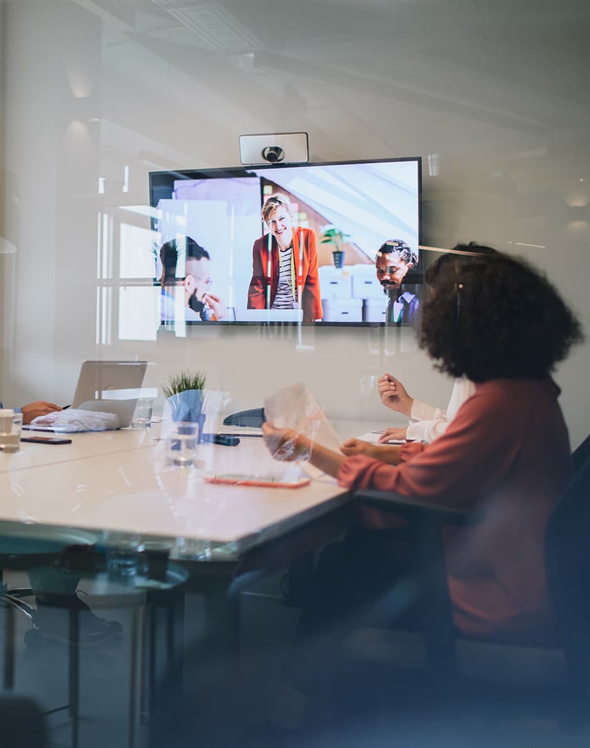 Konferenzraum mit drei Personen, die auf einem großen Bildschirm videotelefonieren
