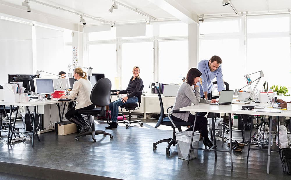 Mitarbeitende in einem Büro mit Computern und Bildschirmen an Schreibtischen