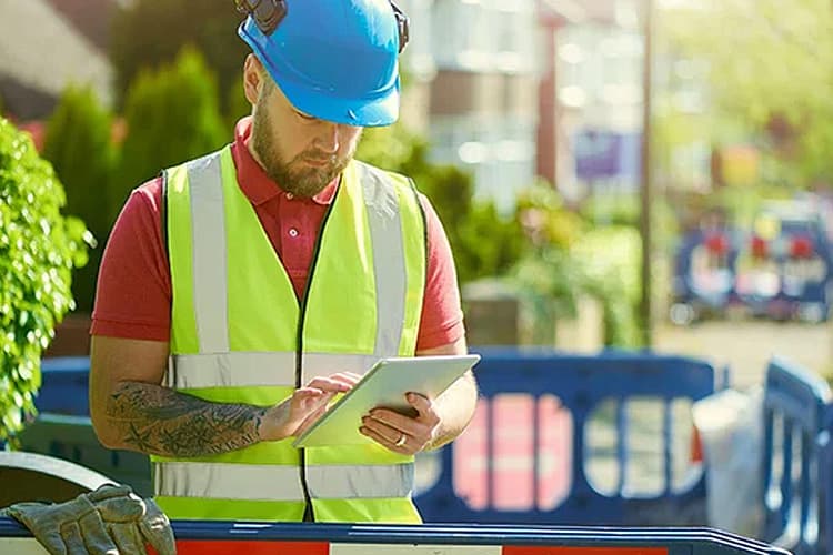 Mann mit Helm und Warnweste schaut auf ein Tablet