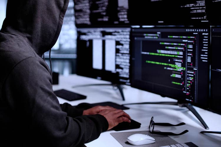 Eine Person im dunklen Hoodie, die Codes an dunklen Bildschirmen eingibt