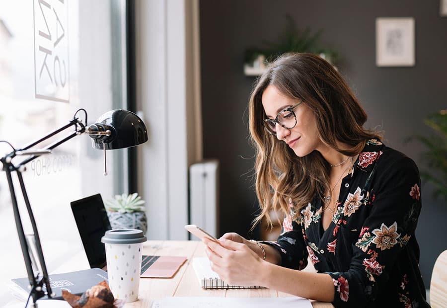 Eine Frau mit Smartphone an einem Schreibtisch mit Computer