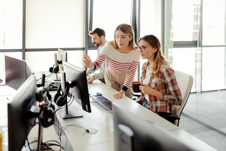 Zwei junge Frauen, die in einem Büro an einem Computerbildschirm etwas besprechen