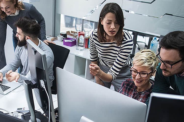 Mehrere Menschen im Büro schauen gemeinsam auf Computerbildschirme