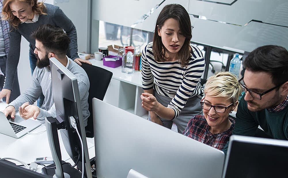 Mehrere Menschen im Büro schauen gemeinsam auf Computerbildschirme