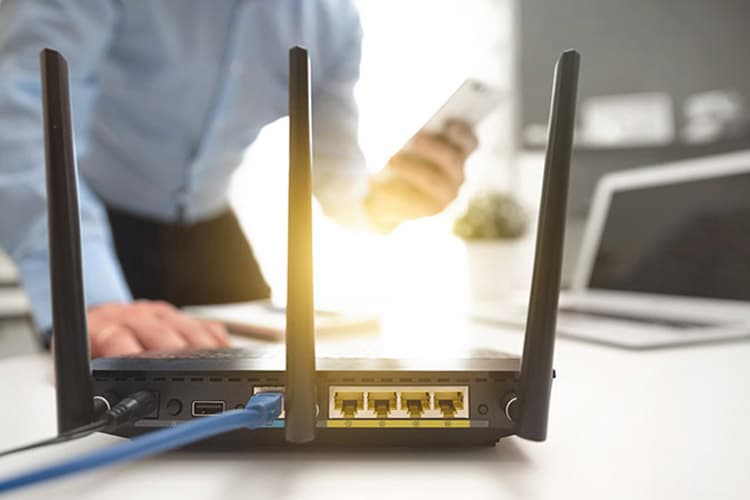 Ein schwarzer Router, im Hintergrund die Silhouette eines Manns mit Handy in der Hand