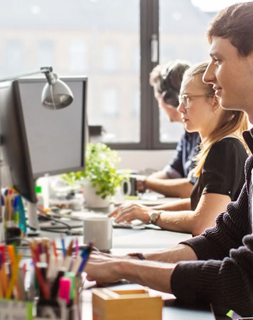 Drei Personen sitzen nebeneinander an Schreibtischen und schauen auf ihre Bildschirme.