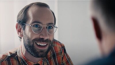 Mann mit Brille und Bart unterhält sich mit einer von hinten gezeigten anderen Person