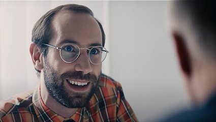 Mann mit Brille und Bart unterhält sich mit einer von hinten gezeigten anderen Person