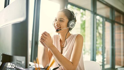 Freundliche Frau mit Headset berät am Telefon vor dem Computer
