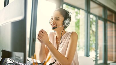 Freundliche Frau mit Headset berät am Telefon vor dem Computer
