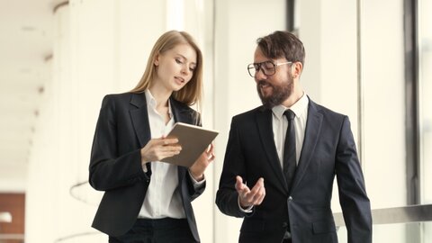 Mann und Frau im Business-Look schauen gehend auf ein Tablet