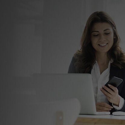 Frau mit Handy in der Hand vor dem Laptop