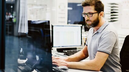 Mann mit Brille in Großraumbüro am Computer