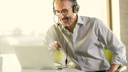 Mann im Hemd mit Headset am Laptop