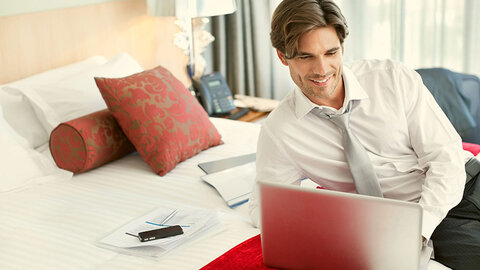 Mann liegt mit Laptop auf Hotelbett