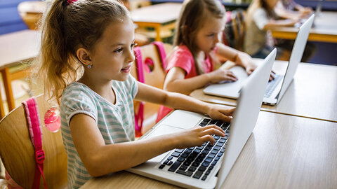 Zwei Mädchen an Schultischen mit Laptops