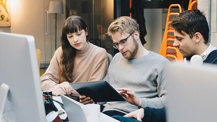 Drei Personen schauen auf ein Laptop im Büro