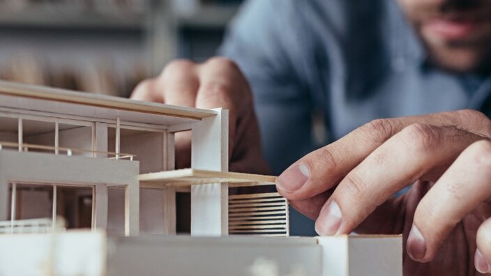 Ein Mann im blauen Hemd setzt vorsichtig Teile in einem Architekturmodell ein.