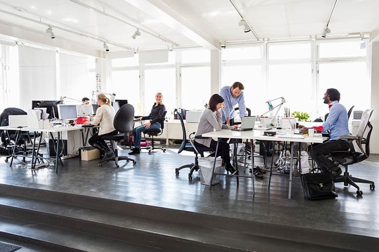 Mitarbeitende in einem Büro mit Computern und Bildschirmen an Schreibtischen