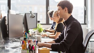 Standortvernetzung von EWE Mehrere Personen an Schreibtischen in Büro schauen auf Bildschirme