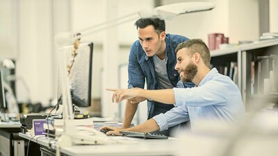 Managed Service von EWE Zwei Kollegen schauen gemeinsam auf einen Bildschirm